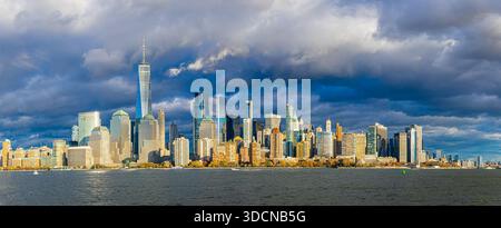 Großer Panoramablick auf die Skyline von Lower Manhattan über den Hudson mit sonnendurchfluteten Türmen unter Sturmwolken; ideal für Reisemarketing, Finanzen, Immobilien Stockfoto
