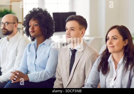Gruppe von Geschäftsleuten, die in einer Besprechung im Büro nebeneinander sitzen und ihren Kollegen zuhören Stockfoto