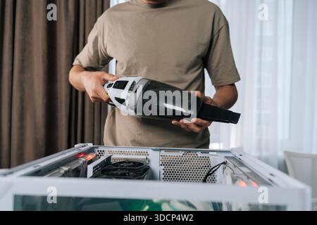 Zugeschnittene Aufnahme eines Mannes, der interne Komponenten des Desktop-Computers mit einem tragbaren Staubsauger reinigt, um optimale Leistung zu gewährleisten und die Hardware zu erweitern Stockfoto