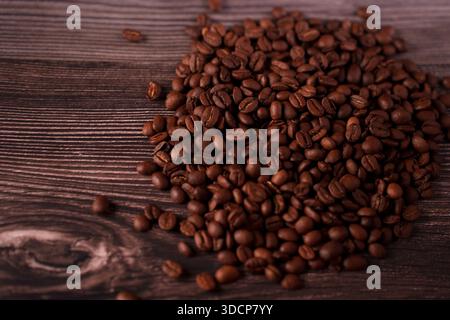 Aus nächster Nähe sehen Sie reichhaltige, geröstete Kaffeebohnen, die elegant auf einer strukturierten Holzoberfläche verteilt sind und komplizierte Details und eine warme, einladende Atmosphäre hervorheben Stockfoto