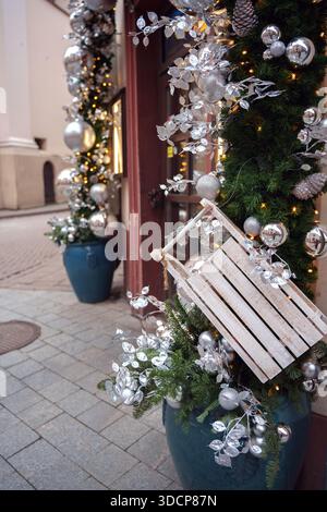 Festliches Straßendekor mit silbernen Ornamenten und Kieferngrün in großen blauen Töpfen, verstärkt durch warme leuchtende Lichter, die eine gemütliche und elegante Atmosphäre schaffen Stockfoto