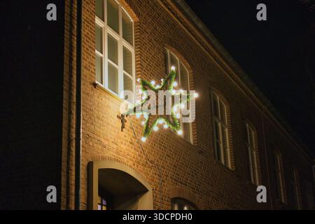 Weihnachtssterndekoration an der Backsteinfassade bei Nacht, festliche Weihnachtsbeleuchtung auf traditioneller europäischer Architektur Stockfoto