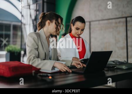 Zwei Frauen arbeiten an einem Laptop-Schreibtisch in einem modernen Büro zusammen, tauschen Ideen aus und planen ein Projekt Stockfoto