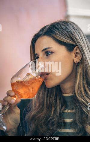 Junge Frau trinkt einen Cocktail in einer Bar, entspannter und nachdenklicher Ausdruck. Lifestyle- und Freizeitkonzept mit Kopierraum für Text. Stockfoto