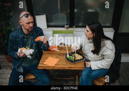 Zwei Freunde teilen sich eine zwanglose Mahlzeit in einem Café im Freien, unterhalten sich und genießen das Essen. Stockfoto