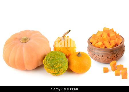 Diese lebendige Studioaufnahme zeigt eine Vielzahl ganzer Kürbisse sowie eine Tonschale mit frischen Orangenwürfeln. Stockfoto