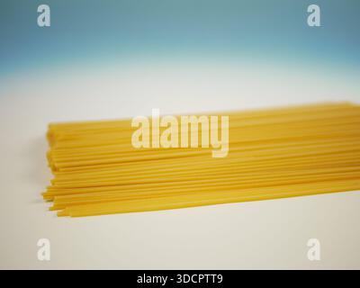 Ungekochte Spaghetti-Nudeln, die in einer flachen Schicht auf weißer Oberfläche mit blauem Farbverlauf verteilt sind, minimales Lebensmittelbild von trockenen italienischen Nudeln und Kochen Stockfoto