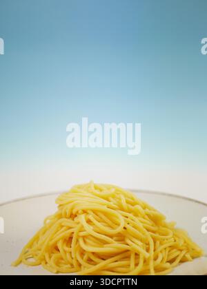 Gekochte Spaghetti, serviert auf einer weißen Teller vor einem klaren blauen Hintergrund mit Farbverlauf, einfache minimale Lebensmittelzusammensetzung für Zutaten oder Mahlzeiten, Profi Stockfoto