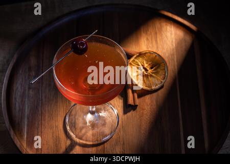 Wunderschöne Beleuchtung auf einem negroni- oder manhattan-Cocktail serviert mit einer Kirsch- und Orangenscheibe. Die Beleuchtung ist dramatisch und warm. Stockfoto