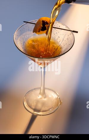 Wunderschöner Bernsteincocktail, ein Negroni oder manhattan, der in ein Martini-Glas mit dramatischer Beleuchtung gegossen wird. Stockfoto
