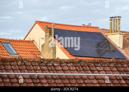 Eine Dachterrasse mit installierten Solarpaneelen, umgeben von traditionellen roten Ziegeldächern und Schornsteinen Stockfoto