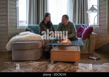 Ein älteres Paar sitzt zu Hause auf dem Sofa und verbringt Zeit miteinander, um Schach zu spielen, sich zu unterhalten und sich in einem gemütlichen Wohnzimmer zu entspannen. Freizeitaktivitäten Zu Hause Stockfoto