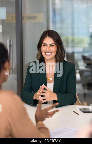 Glückliche, selbstbewusste hispanische Geschäftsfrau, die mit einer Kollegin spricht Stockfoto