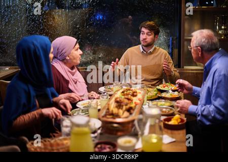 Die muslimische Familie genießt während des Ramadan iftar in einem Restaurant mit warmer Beleuchtung und Dekoration Stockfoto