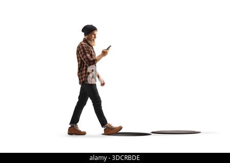 Junger Mann in kariertem Hemd und Jeans, der ein Handy benutzt und auf ein offenes Mannloch läuft, isoliert auf weißem Hintergrund Stockfoto