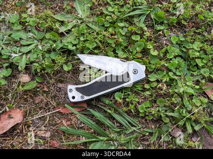 Klappmesser mit rutschfestem Griff auf Schmutz und Blättern. Mehrzweckwerkzeug für Wanderungen und Outdoor-Aktivitäten in der Natur Stockfoto