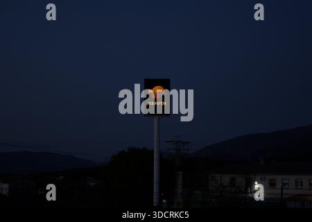 Redaktionelles Foto des beleuchteten Repsol-Schildes in der Abenddämmerung im ländlichen Spanien mit Dorfgebäuden Bergen und dunkelblauem Himmel, das die alltägliche Energieinfrastruktur zeigt Stockfoto