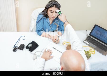 Männlicher Arzt, der die Temperatur mit der Waffe auf den Patienten abnimmt. Arzt misst Temperatur mit Infrarot-Pistole an weibliche Patientin, Doktor misst Temperatur, um zu wom Stockfoto