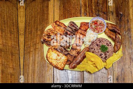 Gegrillte Fleischsorten mit Reis, gebratenem Käse und Tomatensalat, Teller mit verschiedenen Grillsorten auf Holztisch, traditionelles Nicaragua Stockfoto