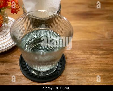 Ein Glas frisches, klares Trinkwasser, serviert in einem stilvollen gerippten oder geriffelten Becher. Das Getränk vermittelt Reinheit, Feuchtigkeit und gemütliche Atmosphäre. Stockfoto