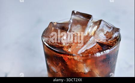 Erfrischendes Foto von Glas gefüllt mit dunklem kohlensäurehaltigem Cola-Erfrischungsgetränk und kristallklaren Eiswürfeln. Das Glas ist mit frischem Kondensationswasser-dro bedeckt Stockfoto
