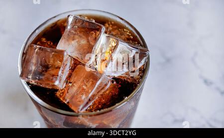 Erfrischendes Foto von Glas gefüllt mit dunklem kohlensäurehaltigem Cola-Erfrischungsgetränk und kristallklaren Eiswürfeln. Das Glas ist mit frischem Kondensationswasser-dro bedeckt Stockfoto