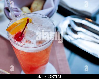 Ein lebendiger, erfrischender Punsch aus roten Früchten oder Cocktail, serviert in einem hohen Glas. Ähnelt einem Mai Tai, Tequila Sunrise oder Erdbeermocktail, gefüllt mit Crys Stockfoto