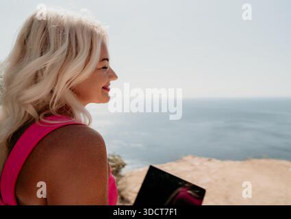 Blonde Frau lächelt mit Laptop im Ozean an Stockfoto