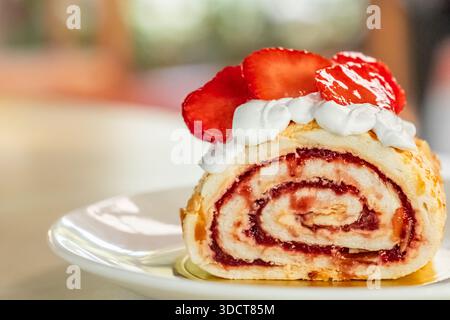 Schwamm-Beerenrolle auf dem Teller mit unscharfem Hintergrund, Nahaufnahme. Tortenscheibe Creme mit Erdbeere. Erdbeerroulade, Kopierraum, niemand Stockfoto