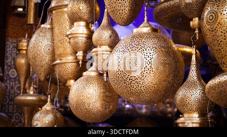 Marokkanische Messinglampen mit feinen Gravuren hängen in einem traditionellen Fès-Geschäft und zeigen komplizierte Muster unter warmer Beleuchtung. Stockfoto