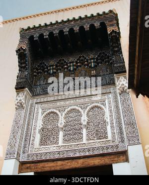 Traditionelle Fassade im maurischen Stil in Fès, verziert mit geschnitztem Stuck, arabischer Kalligraphie und fein gearbeiteten Holzarbeiten unter einem Holzüberhang. Stockfoto