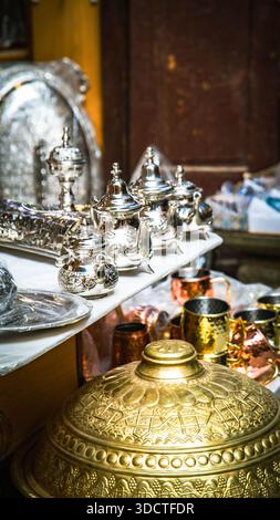 Marokkanische Handwerkskunst in Fès: Fein gravierte silberne Teekannen, Tabletts, goldene Deckel und kupferne Becher in einem traditionellen Geschäft. Stockfoto