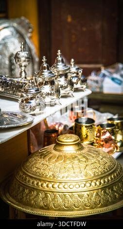 Marokkanische Handwerkskunst in Fès: Fein gravierte silberne Teekannen, Tabletts, goldene Deckel und kupferne Becher in einem traditionellen Geschäft. Stockfoto