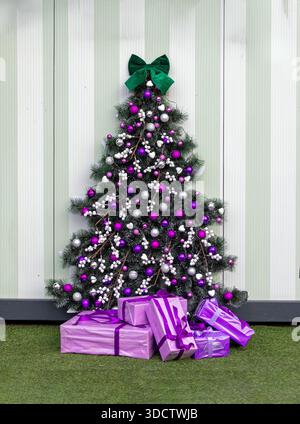 Geschmückter Weihnachtsbaum mit lila Ornamenten und einem Stapel von Geschenken unter dem Zimmer Stockfoto