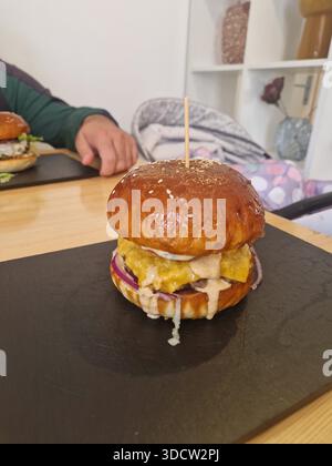 Hausgemachter Cheeseburger, serviert auf einem schwarzen Schieferbrett, mit geschmolzenem Käse, roten Zwiebeln, Sesambrötchen und cremiger Sauce. Stockfoto