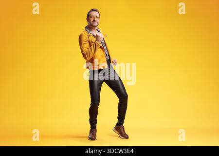 Stilvoller Mann im Retro-Disco-Outfit, der vor gelbem Hintergrund tanzt Stockfoto