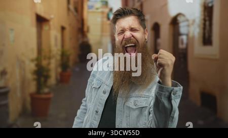 Mann mit Bart beugt sich nach vorne, hebt geballte Faust und ruft in der sonnendurchfluteten Altstadtstraße; Aufregung. Stockfoto