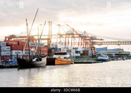 Lissabon Portugal 6. Dezember 2025. Historische Segelschiffe und orangene Arbeitsboote liegen in der Nähe von gestapelten Schiffscontainern und Kränen an einem Flusshafen in Stockfoto