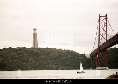 Lissabon Portugal 6. Dezember 2025. Ein kleines Segelboot fährt über den Tejo unter der Brücke Ponte 25 de Abril mit dem Cristo Rei-Denkmal im B Stockfoto