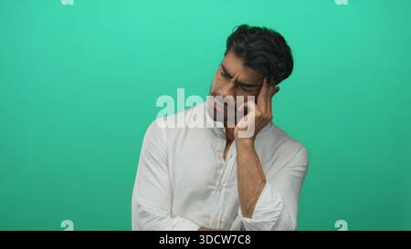 Der Mann drückt die Fingerspitzen, um in nachdenklicher Pose in grünem Studio mit sanfter Richtungsbeleuchtung zu kneifen; Verwirrung. Stockfoto