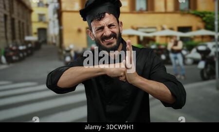 Bärtiger hispanischer Mann, der als Koch gekleidet ist und Boxpositionen auf der Straße im Freien nachahmt und professionelle Kleidung mit spielerischem Ausdruck verbindet. Stockfoto