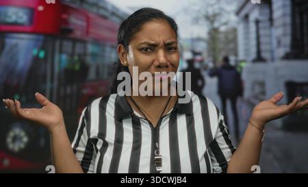 Die Schiedsrichterin zuckt Palmen auf der belebten Straße vor einem vorbeifahrenden roten Bus und verschwommenen Fußgängern; Unsicherheit. Stockfoto