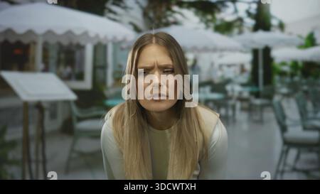 Frau sitzt auf der Außenterrasse im Stadtcafé mit einem durchdachten Ausdruck in eleganter Restaurantatmosphäre. Stockfoto