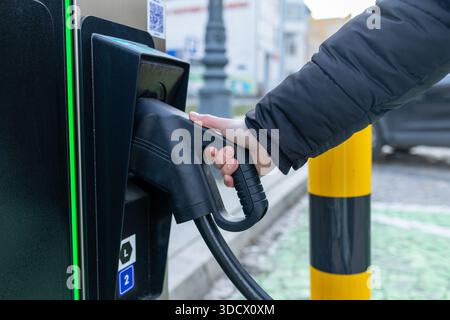 Übergang zu Elektro- und Hybridfahrzeugen, Frau, die ein Elektroauto auflädt, Nahaufnahme der Hand eines Mannes und ein Elektroladestecker Stockfoto