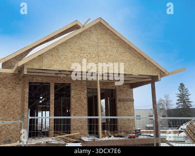 Holzhausrahmen im Bau. Frühes Wohngebäude mit freiliegenden Holzrahmen und Dachstühlen an einem klaren Tag, was Fortschritte zeigt Stockfoto