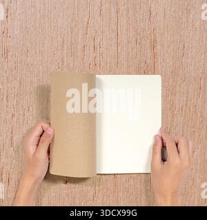 Draufsicht eines offenen Notizbuchs, das von Händen gehalten wird und eine leere Seite zeigt, die für Text oder Design bereit ist. Perfekt für Geschäftspräsentationen oder Schulungen. Modell Stockfoto
