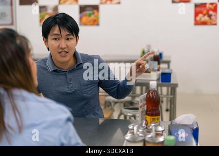 Asiatischer Mann zeigt mit dem Finger, diskutiert und erklärt Konzept im Restaurant Stockfoto