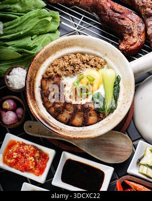 In einer Nahaufnahme aus der Nähe wird ein dampfender Ton-Topf-Reisgericht mit herzhaftem Schweinefleisch gezeigt, ein perfekt gekochtes, sonniges Ei, das in Scheiben geröstet wird Stockfoto