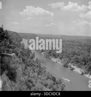 Ukraine, Region Donezk, Sviatohirsk, 1980er Jahre Ein archiviertes Schwarzweißfoto, das einen majestätischen Panoramablick auf den Seversky Donets River von den Kreidefelsen aus macht. Ein kleines Vergnügungsboot fährt entlang des gewundenen Wassers, umgeben von den üppigen dichten Wäldern des Naturschutzgebietes der Heiligen Berge. Diese alte Luftlandschaft vermittelt die ruhige Schönheit des beliebten Resorts. Es dient als wertvolles historisches Dokument der Natur und des Tourismus im friedlichen Donbass vor dem Krieg. Stockfoto