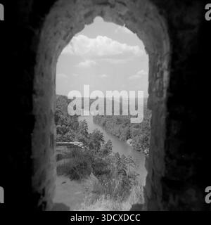 Ukraine, Region Donezk, Sviatohirsk, 1980er Jahre Ein archiviertes Schwarzweißfoto, das einen malerischen Blick auf den Seversky Donets River durch einen Steinbogen auf den Kreidefelsen macht. Der natürliche Rahmen zeigt einen sich windenden Fluss, üppige dichte Wälder und einen bewölkten Himmel, der charakteristisch für das Naturschutzgebiet Holy Mountains ist. Dieses künstlerische Vintage-Bild bewahrt die ruhige Atmosphäre der Landschaft in einem friedlichen Donbass vor dem Krieg und dient als wertvolles historisches Dokument dieser Zeit. Stockfoto